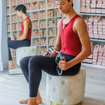 Man in red tank top and black leggings sitting on a white stool in a store setting.