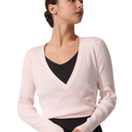 Woman wearing a light pink wrap-style sweater over a black top on a white background