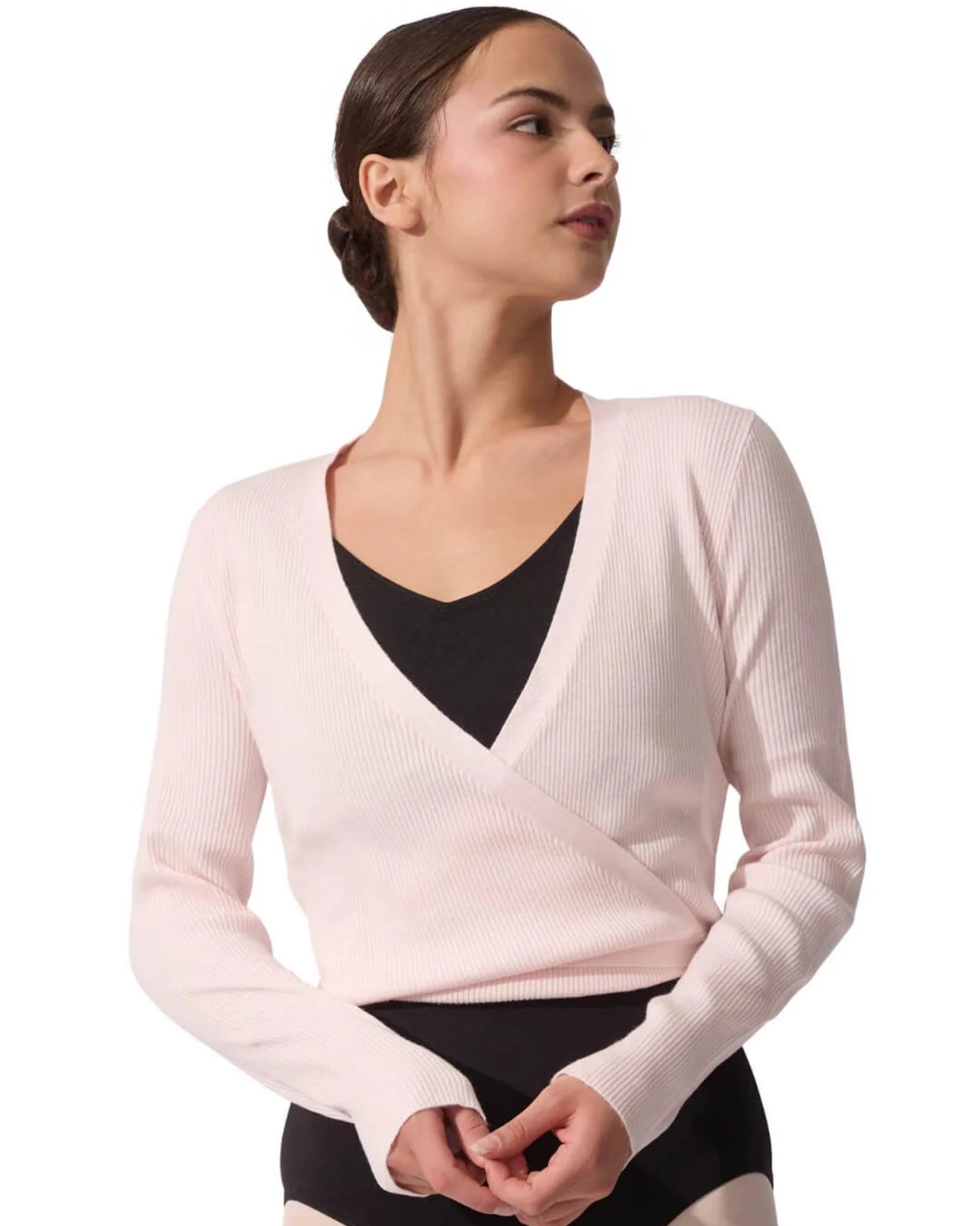 Woman wearing a light pink wrap-style sweater over a black top on a white background