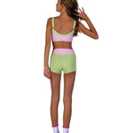 A woman shown from the back wearing a pastel two-piece dance set with a pink and light green polka dot bra topand matching shorts, paired with light purple socks, on a solid white background.