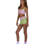 A young girl modeling a matching two-piece activewear set consisting of a pink and green polka dot sports bra and shorts, paired with light purple socks, against a solid white background.
