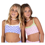 Two young girls modeling matching bra top sets against a plain white background. The girl on the left wears a light purple and white polka dot bra top and bottom with a candy necklace. The girl on the right wear a light pink and light green polka dot bra top and bottom with a candy necklace.