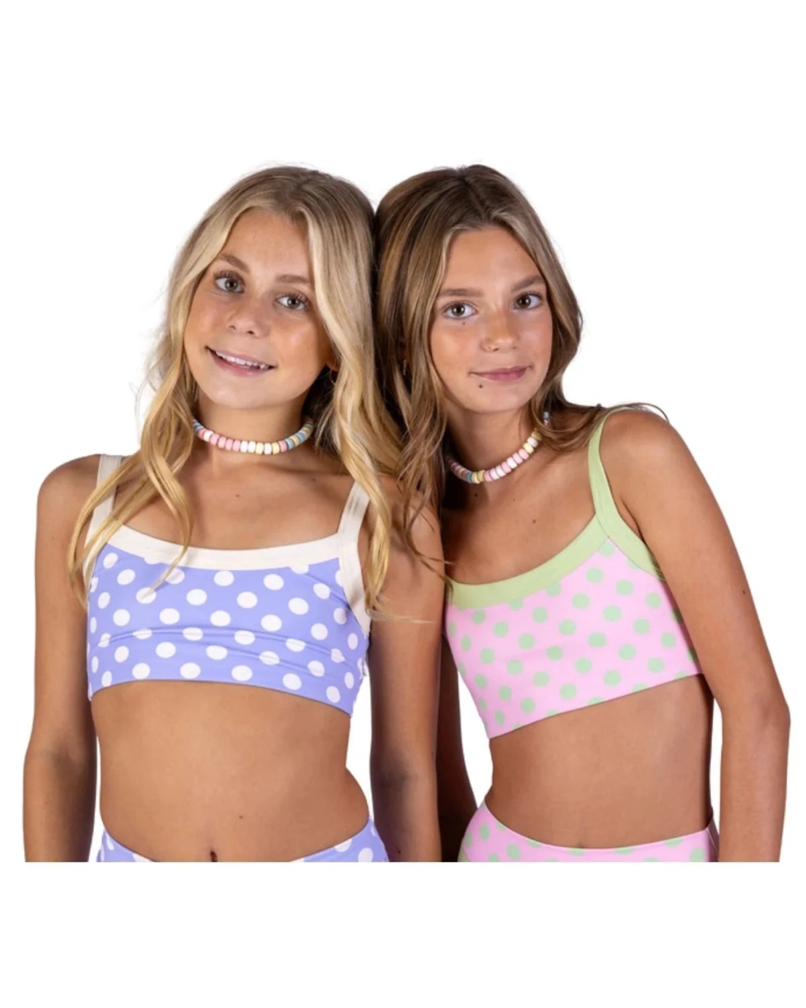 Two young girls modeling matching bra top sets against a plain white background. The girl on the left wears a light purple and white polka dot bra top and bottom with a candy necklace. The girl on the right wear a light pink and light green polka dot bra top and bottom with a candy necklace.