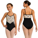 A young girl modeling a black leotard from the front and back against a plain white background. The leotard features a patterned bust panel with nutcracker illustrations on a light beige background and thin black shoulder straps.