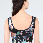 Woman wearing a black sleeveless leotard with colorful floral patterns on a light gray background