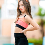 Woman wearing a colorful sports bra and black shorts with an orange sunglasses.