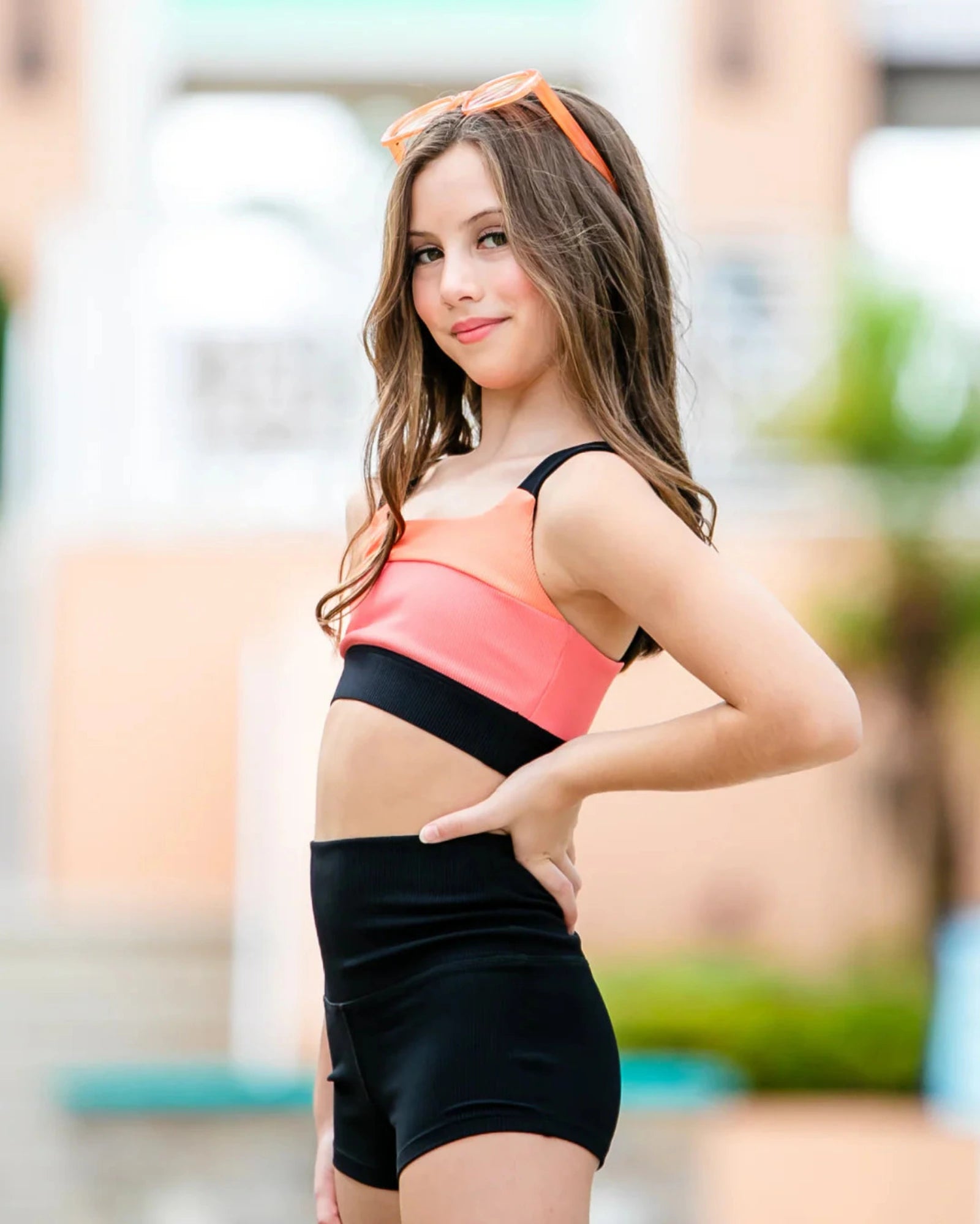 Woman wearing a colorful sports bra and black shorts with an orange sunglasses.