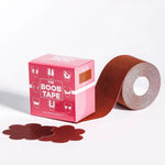 Pink retail box labeled 'THE BOOB TAPE' beside a roll of reddish-brown adhesive tape with several flower-shaped tape pieces in front, photographed on a clean white studio background.