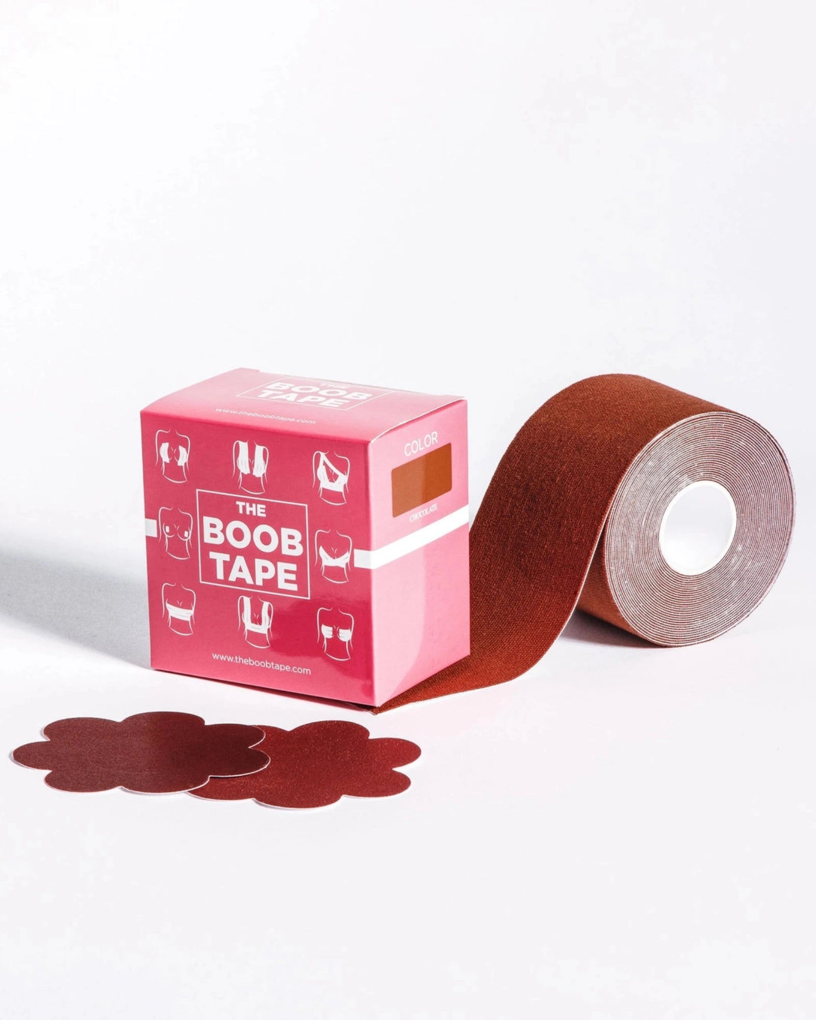 Pink retail box labeled 'THE BOOB TAPE' beside a roll of reddish-brown adhesive tape with several flower-shaped tape pieces in front, photographed on a clean white studio background.