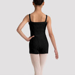 A child dancer shown from the back wearing a black cable-knit unitard, light pink tights, and ballet shoes against a light gray studio background.