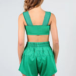 A woman shown from the back wearing a matching green dance set consisting of a cropped tank top with wide shoulder straps and high-waisted shorts with an elastic waistband, against a light gray studio background.