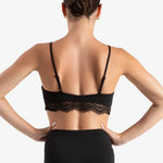 Rear view of a woman wearing a black lace-trimmed dance bra and black leggings against a light gray studio background.