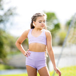 Young girl in a purple dance outfit standing outdoors with trees in the background