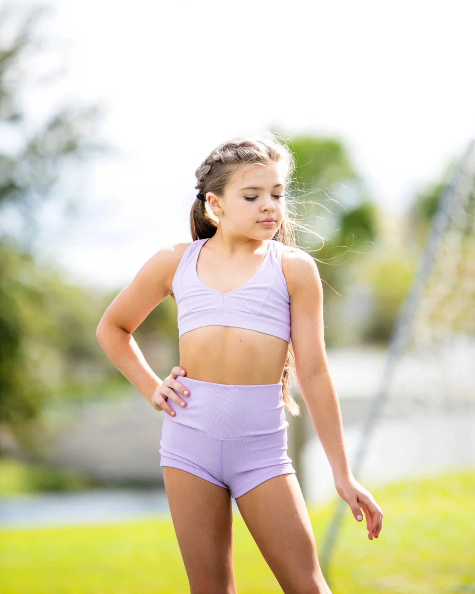 Young girl in a purple dance outfit standing outdoors with trees in the background