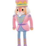A plush nutcracker doll with a pink and lavender outfit, yellow accents, and a white beard, standing against a plain white background.