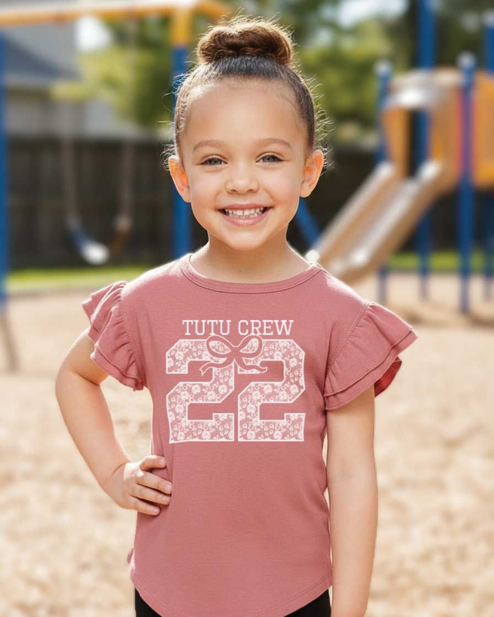 Child wearing a pink shirt with 'Tutu Crew 22' text at a playground