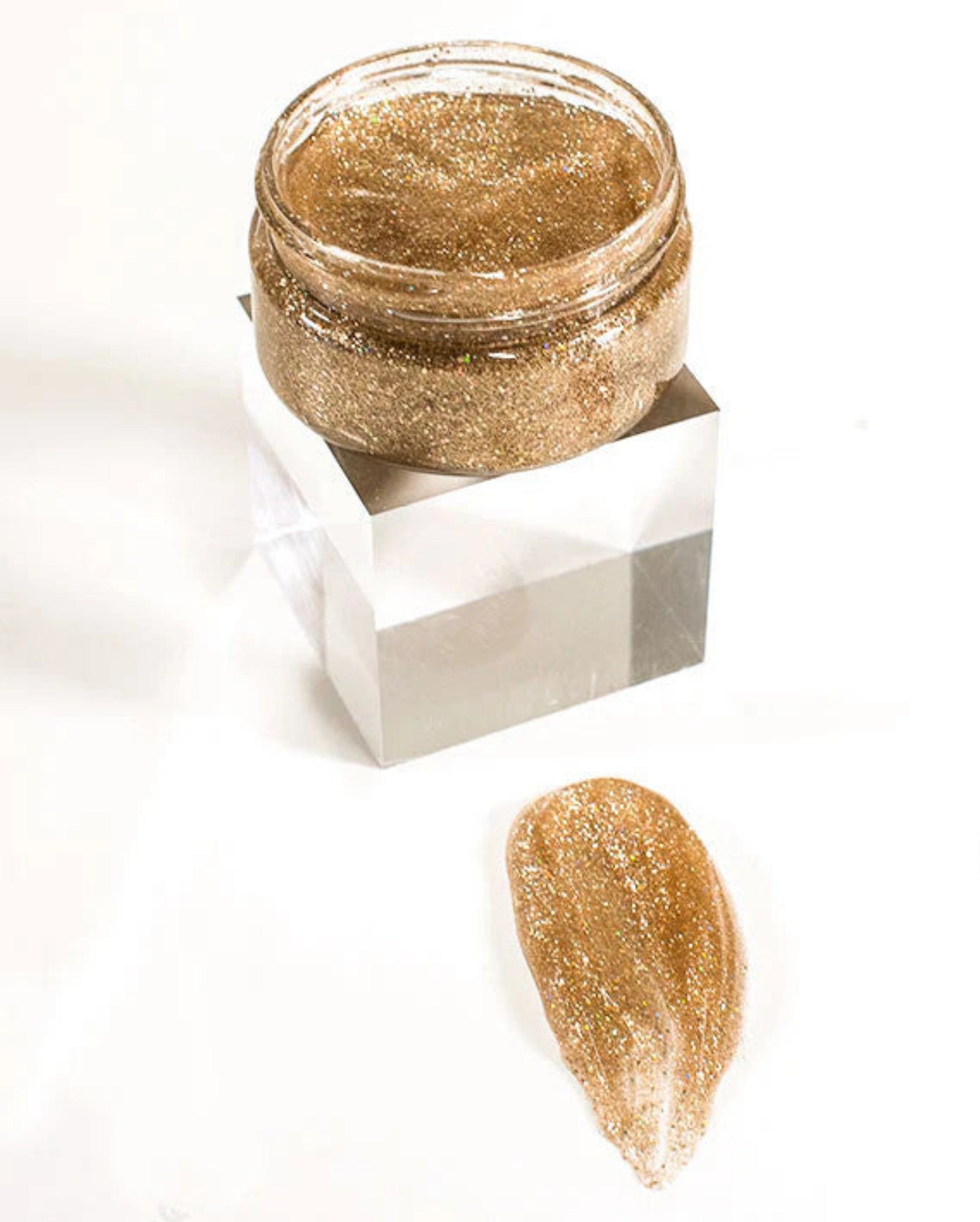 Gold glittery cream in a small jar with a sample on a white background