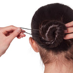 Person styling a bun with hair pins on a white background