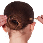 Person adjusting a hair bun with a hairpin on a white background