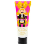 A squeeze tube of hand cream featuring a colorful nutcracker illustration on a pink and yellow harlequin pattern background, with a black flip-top cap, photographed on a plain white background.