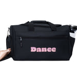 Black dance bag with 'Dance' written on it, next to a pair of pink ballet shoes on a white background.