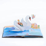 An open 3D pop-up children's book featuring a white swan carrying a Nutcracker and Clara, with a castle, water, and a small angel figure on the illustrated pages against a white background.