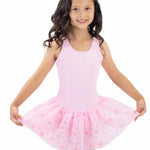 A young girl with long dark curly hair wearing a light pink sleeveless leotard and a matching pink tutu skirt with darker pink flowers, posing against a solid white background.