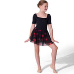 A young girl dancer wearing a black short-sleeve leotard and a black tulle tutu skirt with red strawberries, posed against a solid white studio background.