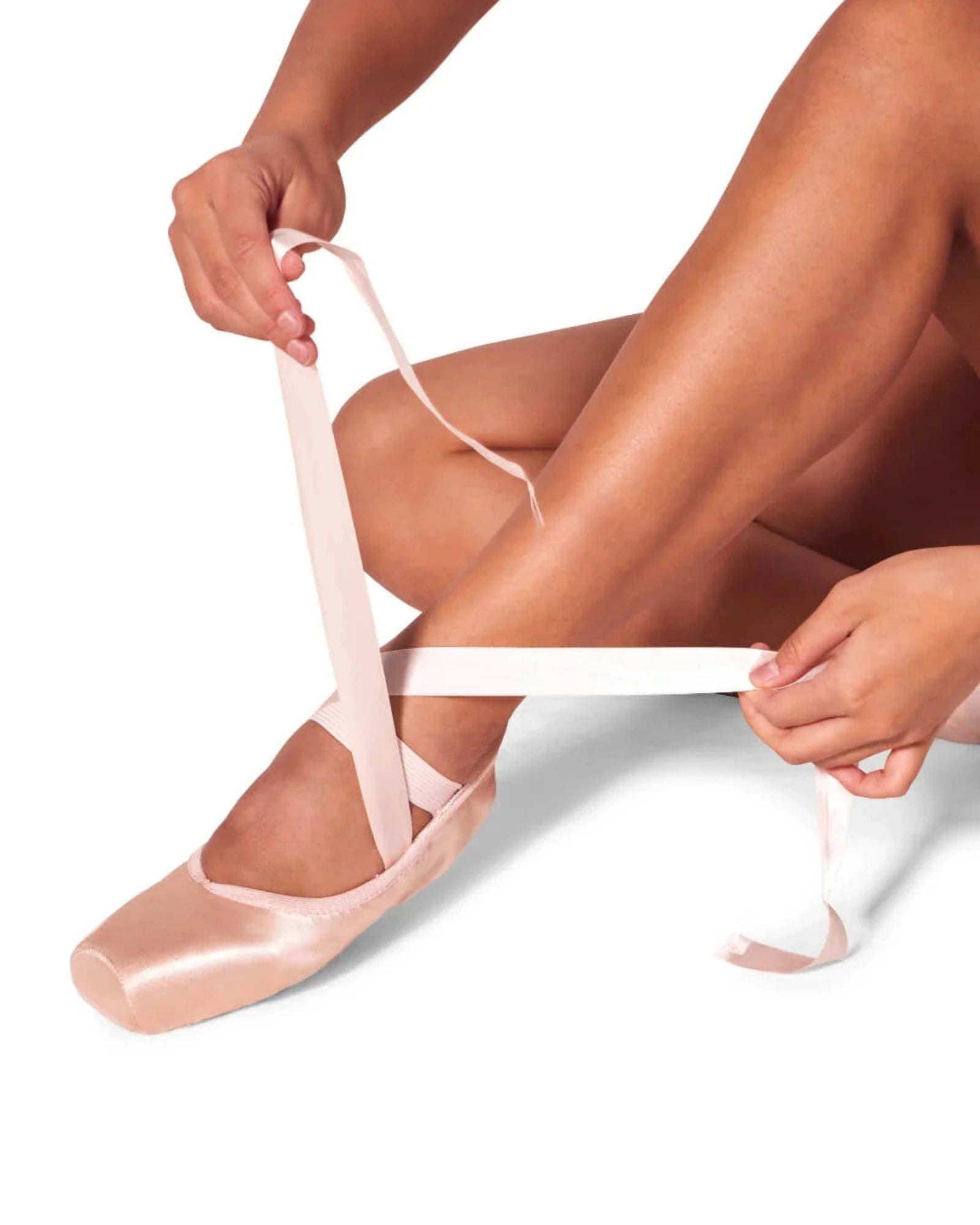 Person wearing ballet shoes with ribbons, sitting on a white background