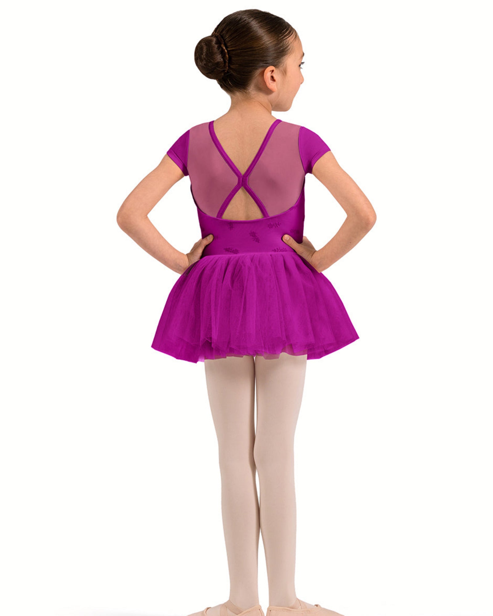 A young girl dancer shown from the back wearing a bright magenta purple short-sleeve leotard with a mesh criss-cross back and a matching tutu skirt, paired with light pink tights and ballet shoes, against a plain white background.