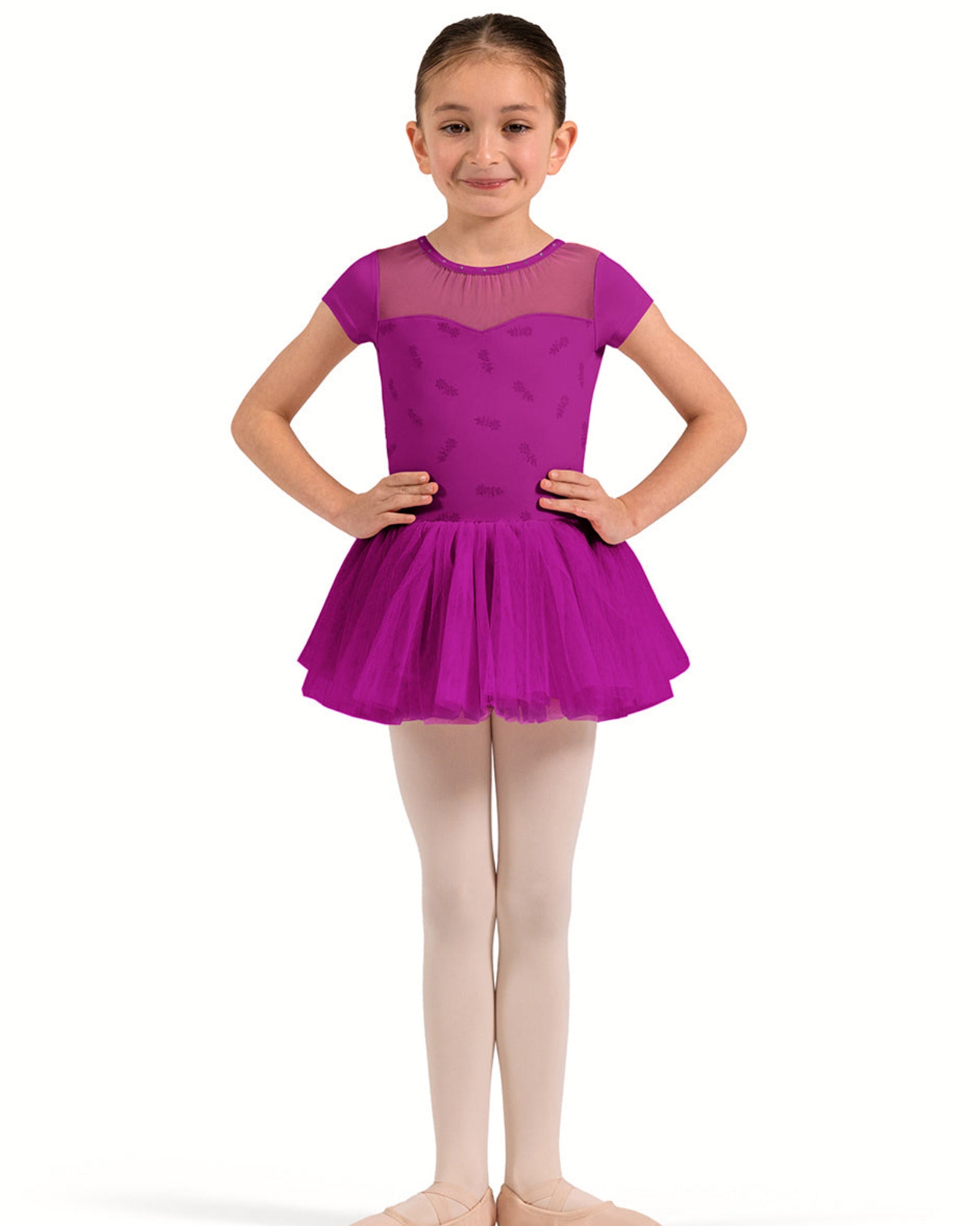 A young girl dancer wearing a bright magenta purple tutu leotard with a sheer mesh yoke, paired with light pink tights and ballet shoes, posing against a solid white background.
