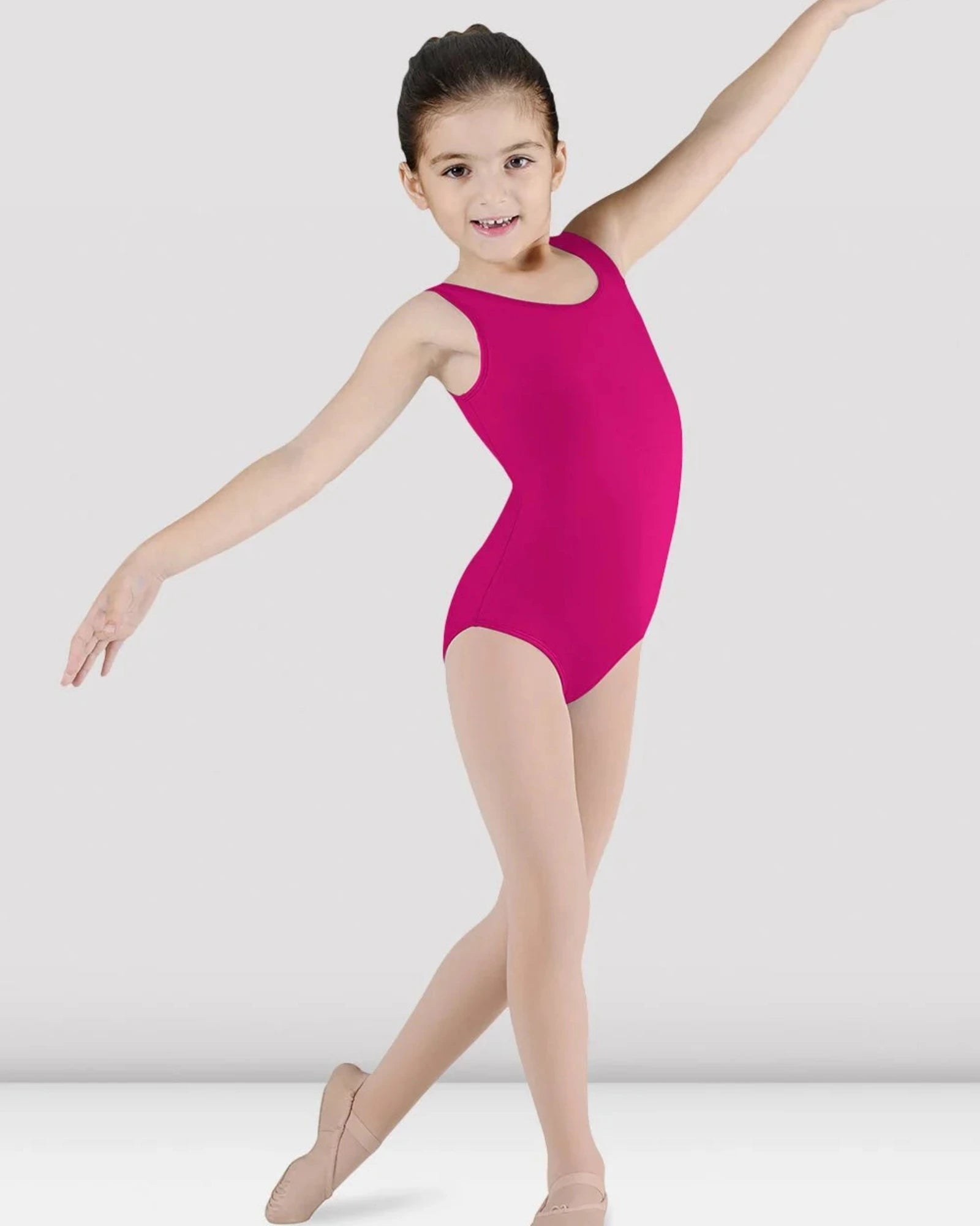 A young girl dancer posing in a bright magenta sleeveless leotard and nude tights against a light gray studio background.