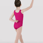 A young girl dancer viewed from behind wearing a bright magenta pink sleeveless leotard and nude tights, posing in a ballet position against a light gray studio background.