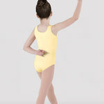 A young girl dancer shown from the back wearing a pale yellow sleeveless leotard and nude tights, posing in a studio setting against a light gray background.