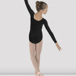 Ballerina in a black leotard and beige tights posing against a white background