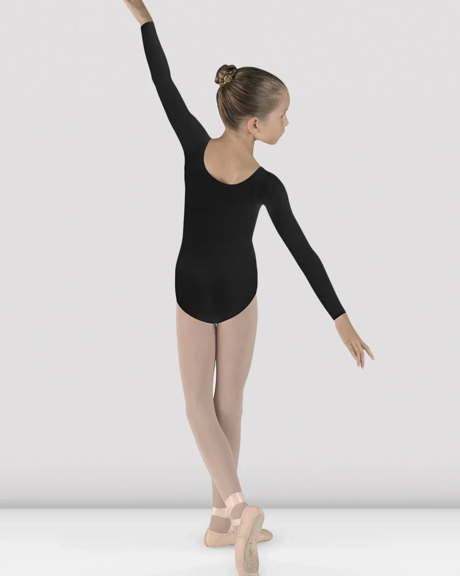 Ballerina in a black leotard and beige tights posing against a white background