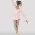 Young dancer in a pink leotard and beige tights posing against a white background