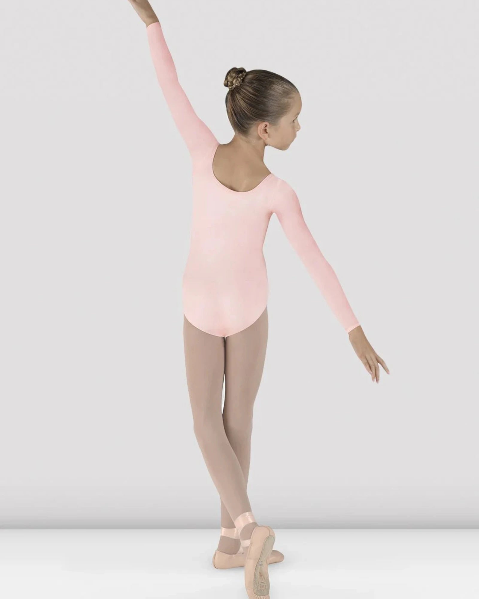 Young dancer in a pink leotard and beige tights posing against a white background