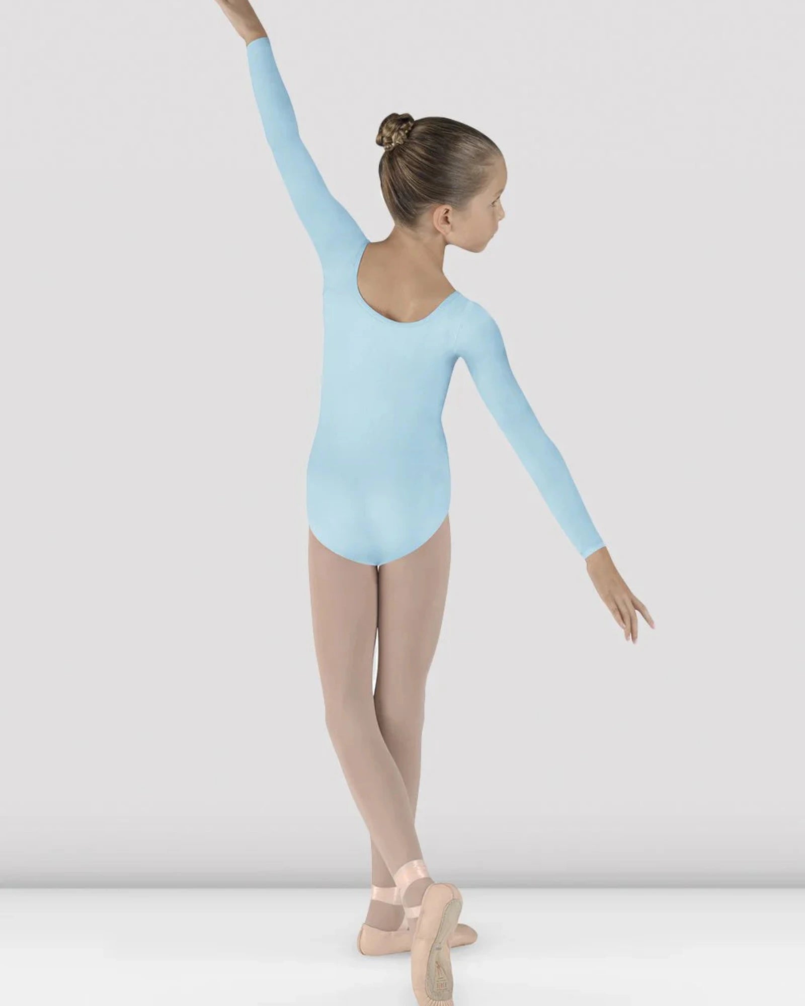 Ballerina in a light blue leotard and beige tights posing against a white background