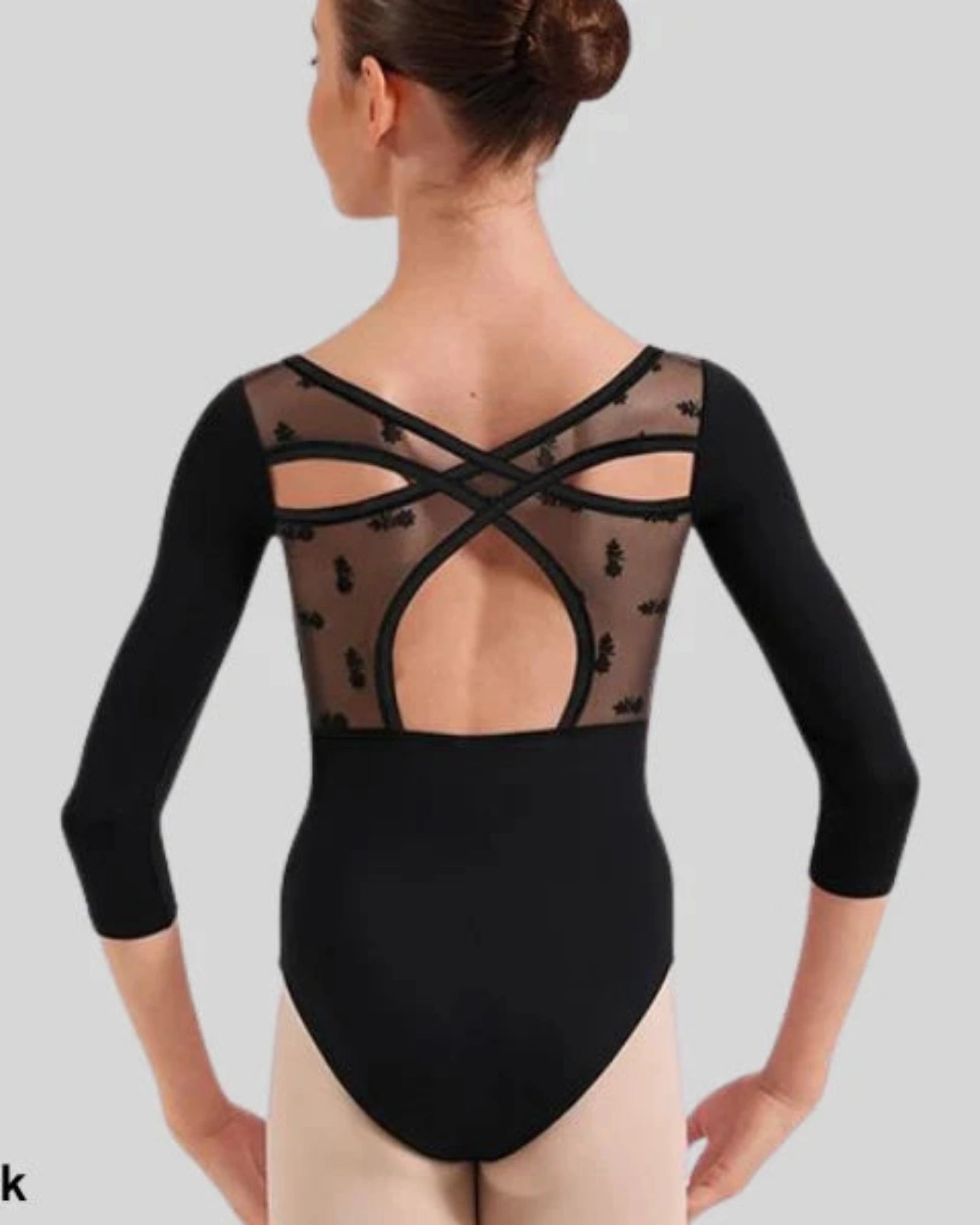 A woman modeling a black three-quarter sleeve dance leotard from the back, showing a sheer mesh back panel with decorative black lace and crisscross straps. 