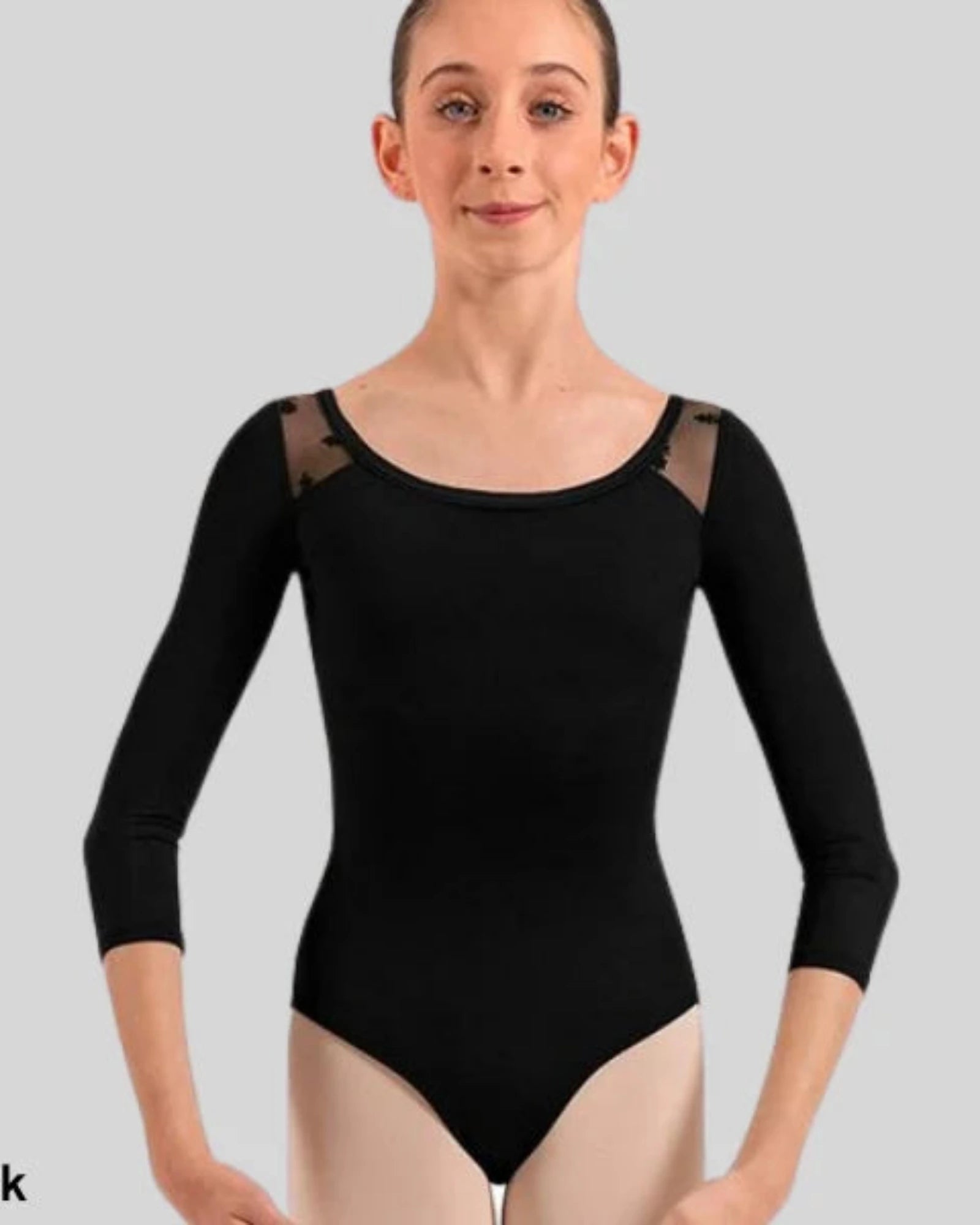 A young gymnast wearing a black 3/4 sleeve leotard with sheer shoulder mesh panels, shown against a solid gray background. 