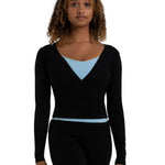 A woman modeling a black long-sleeve wrap-style knit top with a light blue V-neck undershirt and black leggings, shown against a plain white background.