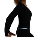 A woman shown in side profile wearing a black ribbed long-sleeve top with a light blue underlayer peeking out at the neckline and waist, paired with black leggings, against a plain white background.