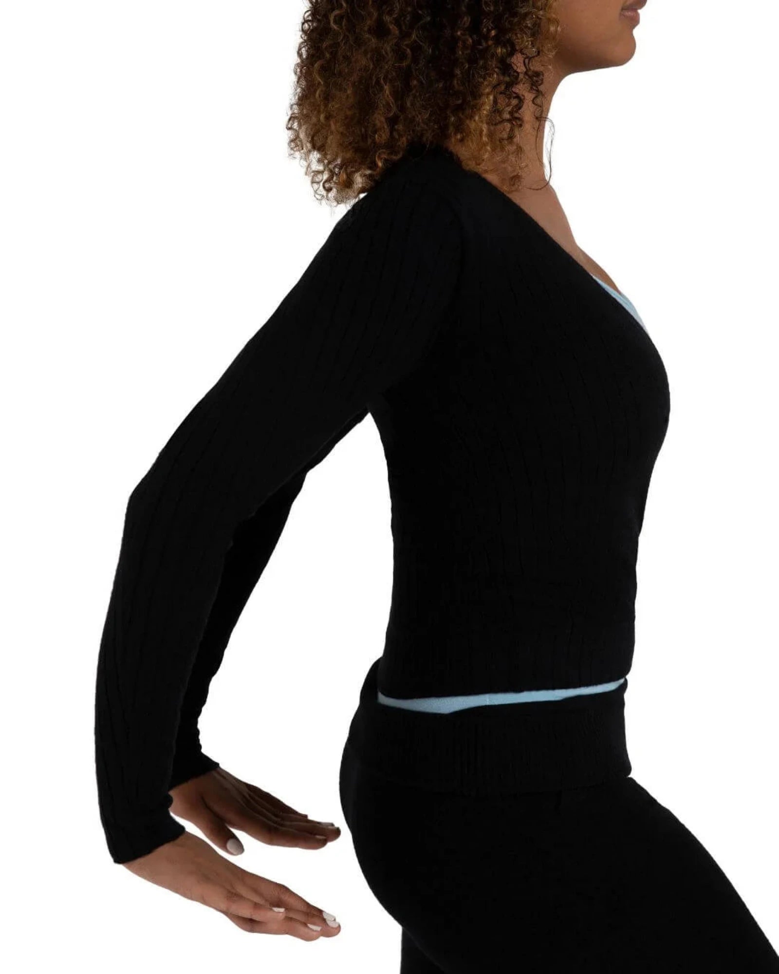 A woman shown in side profile wearing a black ribbed long-sleeve top with a light blue underlayer peeking out at the neckline and waist, paired with black leggings, against a plain white background.