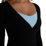 A close-up of a woman wearing a black ribbed long-sleeve V-neck top layered over a light blue scoop-neck undershirt, against a plain white background.