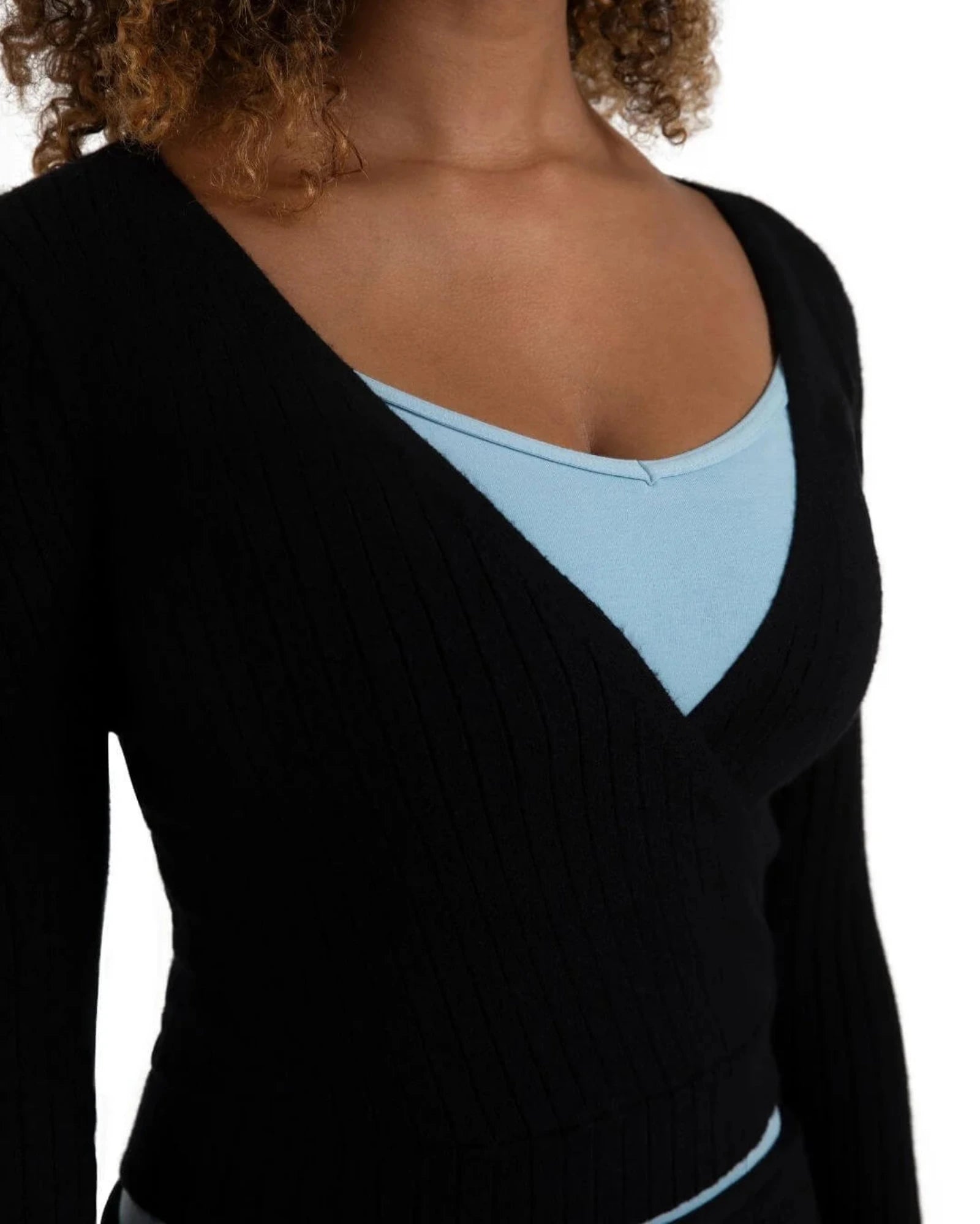 A close-up of a woman wearing a black ribbed long-sleeve V-neck top layered over a light blue scoop-neck undershirt, against a plain white background.