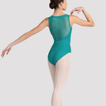 A female dancer shown from the back wearing a teal-green sleeveless leotard with a sheer mesh back panel, paired with light pink tights and pointe shoes, against a light gray studio background.