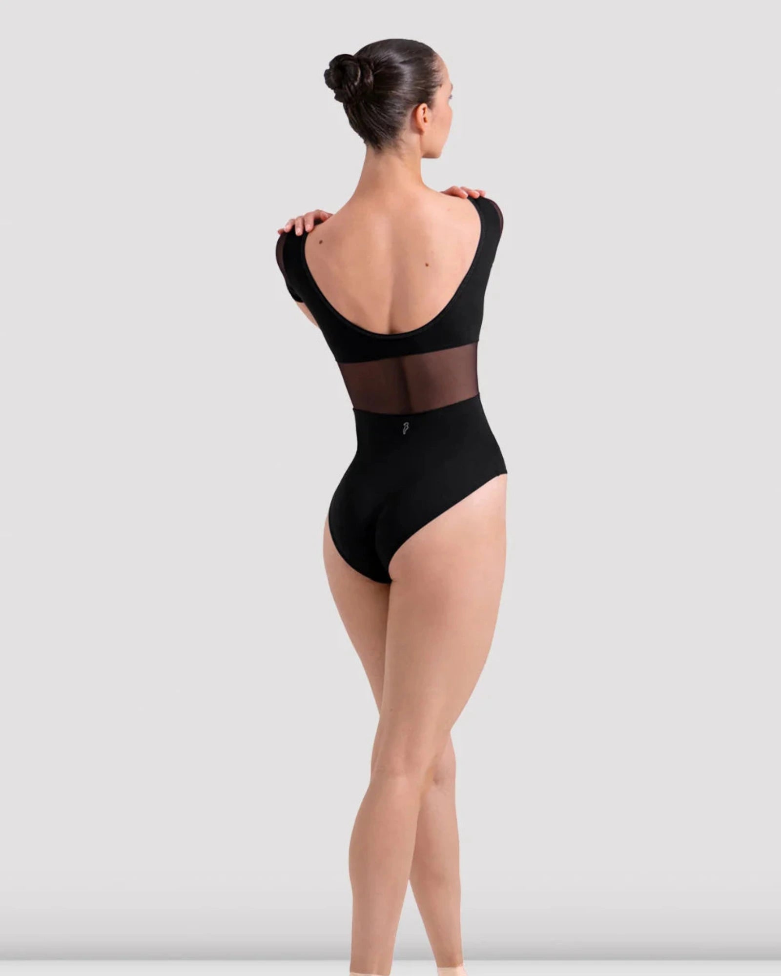 Dancer in a black leotard and ballet shoes on a white background
