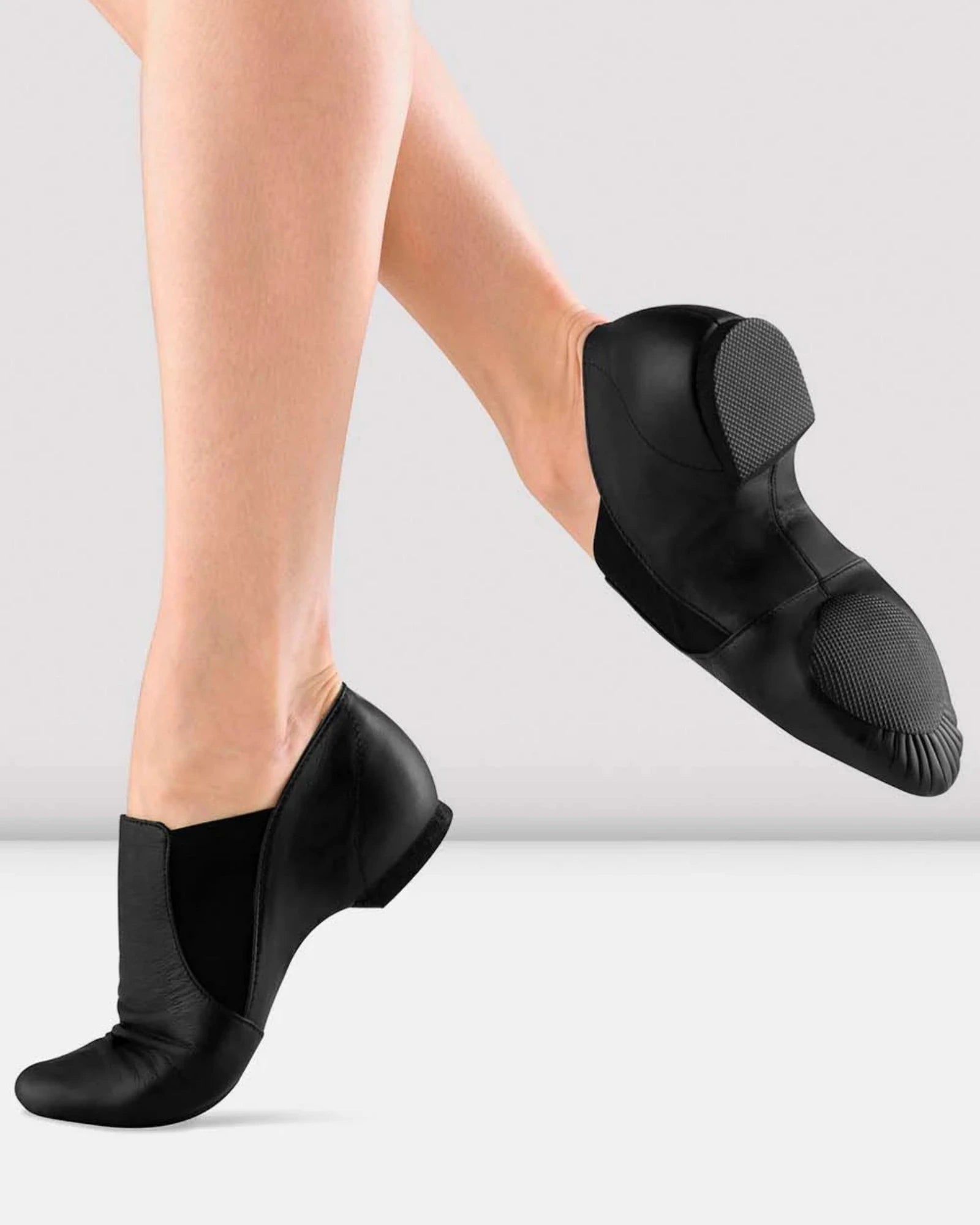 Black slip-on shoes worn by a person on a light gray background