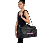 A woman wearing a black tank top and leggings carries a black duffel bag with pink 'Dance' lettering on the front, set against a plain white background.